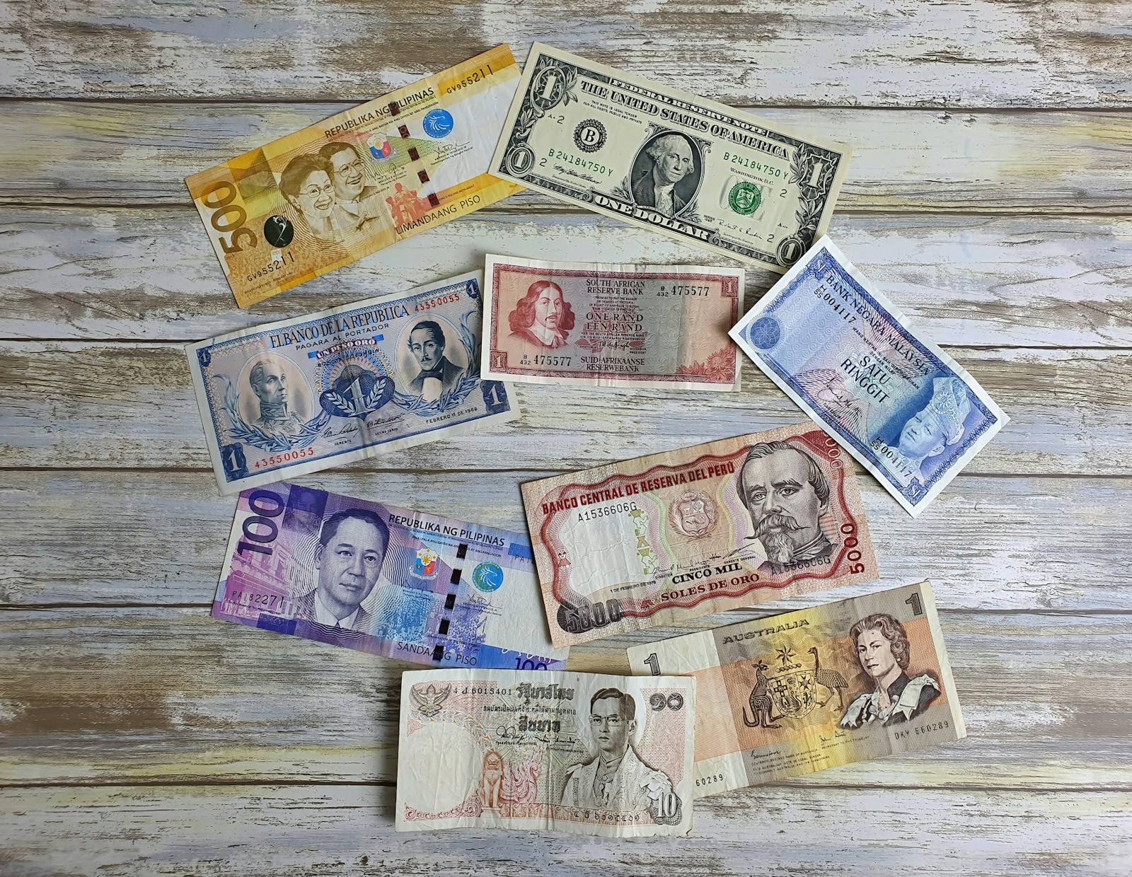 Banknotes from several countries laid out side by side on a wooden table