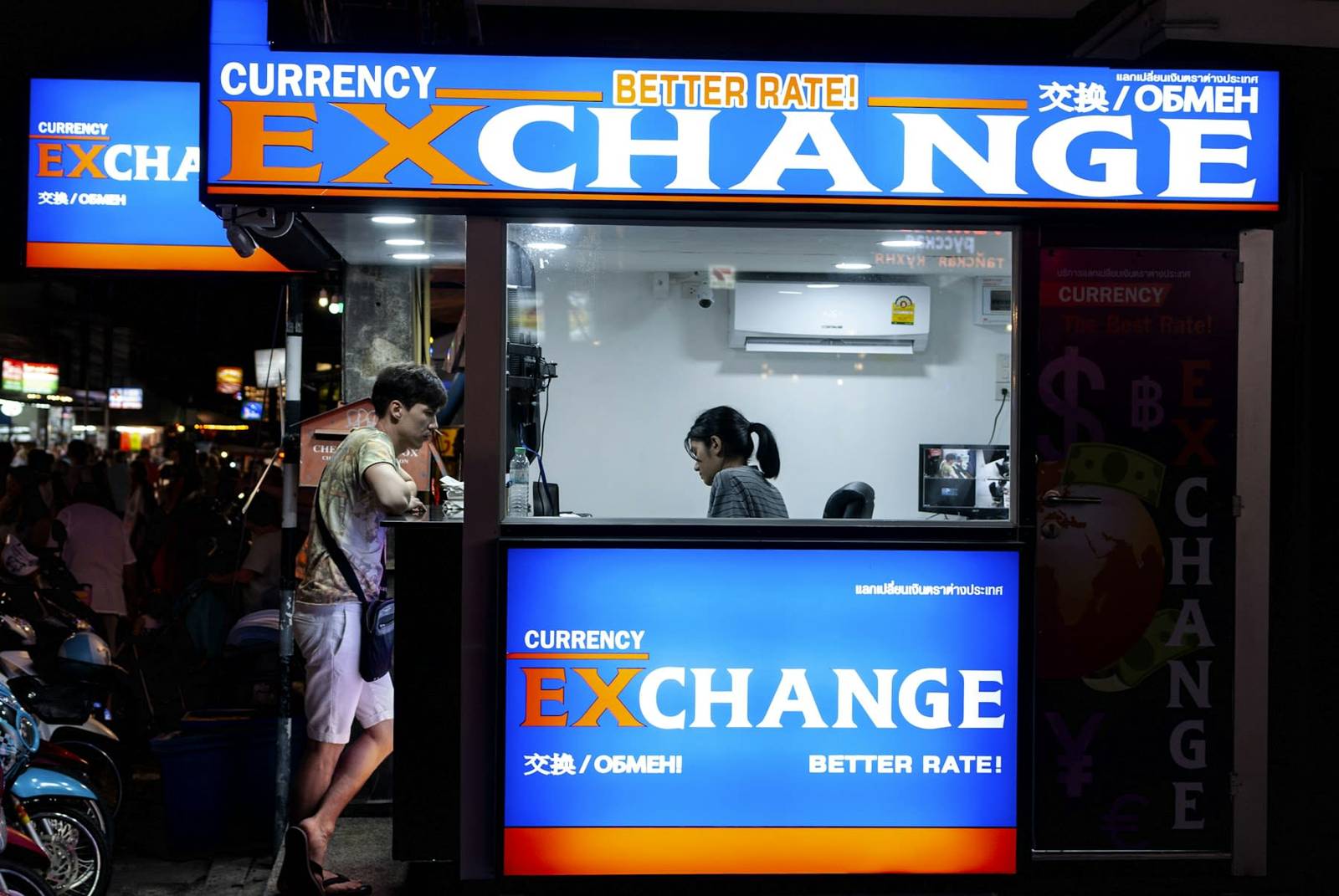 A lit up currency exchange booth on the street with a BETTER RATE sign