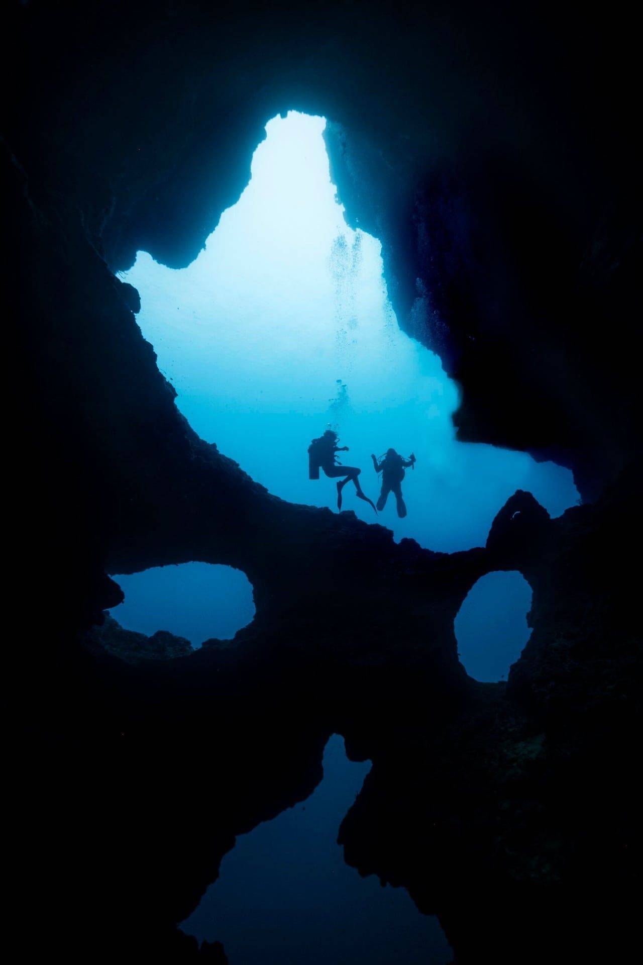 Divers hovering beneath the rock opening of the Cathedral at Pescador Island