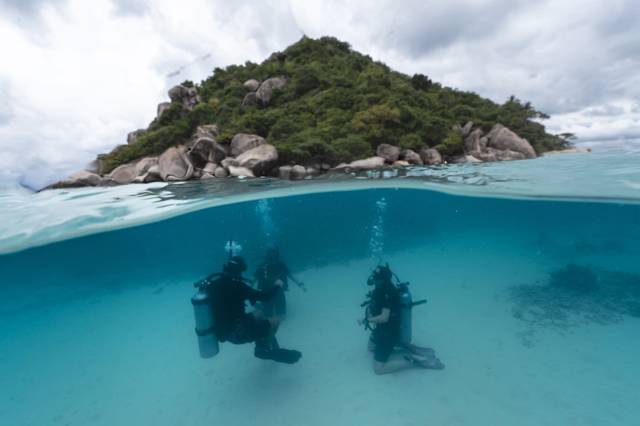 Divers under water at Koh Nang Yuan, with the island above the surface