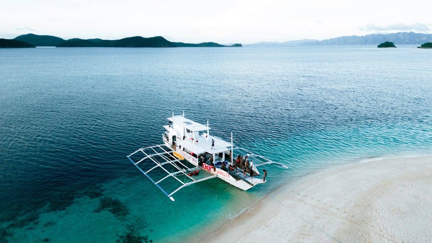 The boat anchored off a white beach on the way to El Nido
