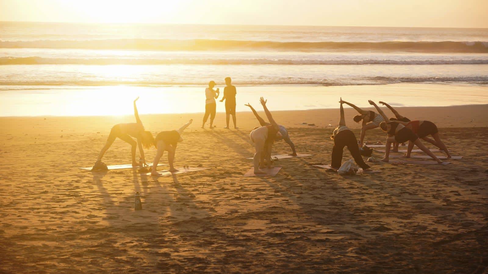 Group doing yoga together on the beach at sunset