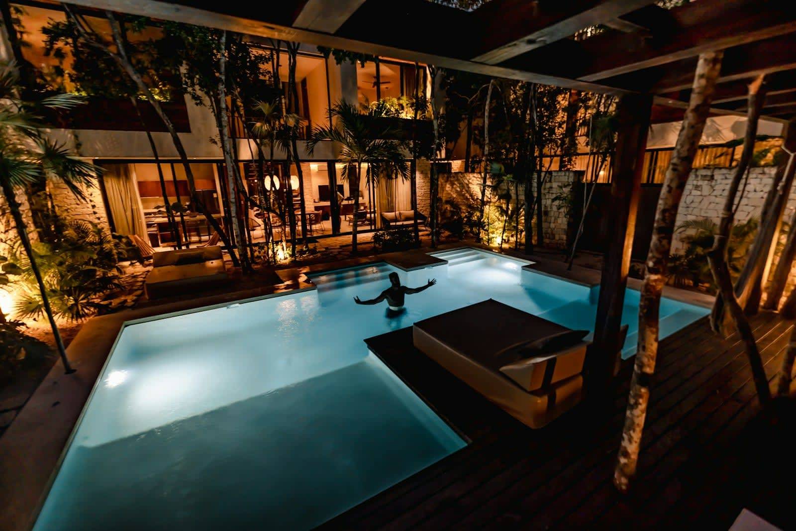 Lit pool at dusk with an open lounge and plenty of greenery around it