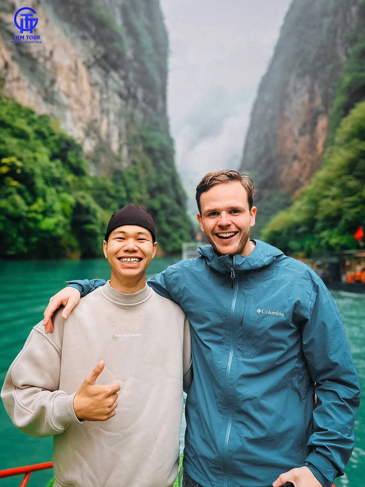 Two travel companions giving a thumbs up on the boat between the cliffs
