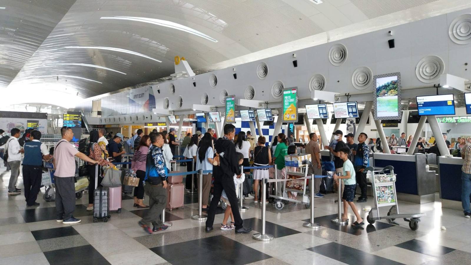 Travellers with luggage trolleys queueing at airport check in desks