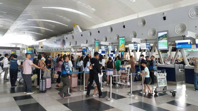 Travellers with luggage trolleys queueing at airport check in desks