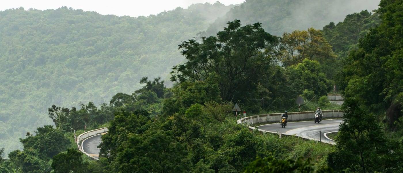 Motorbike riders on a winding mountain road through green hills