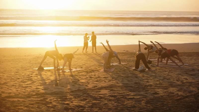 Group doing yoga together on the beach at sunset