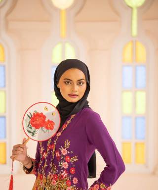 Woman in a headscarf and embroidered traditional dress holding a fan