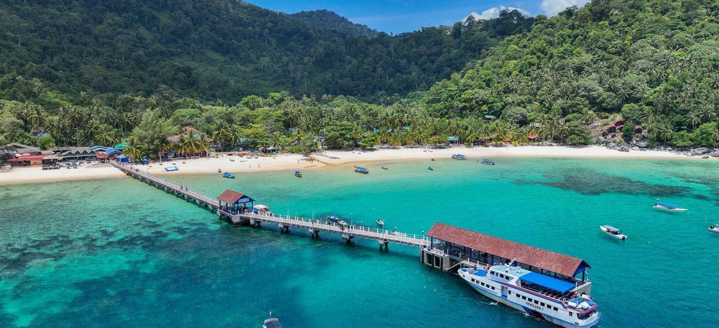 A jetty and white beach on a green island in turquoise water