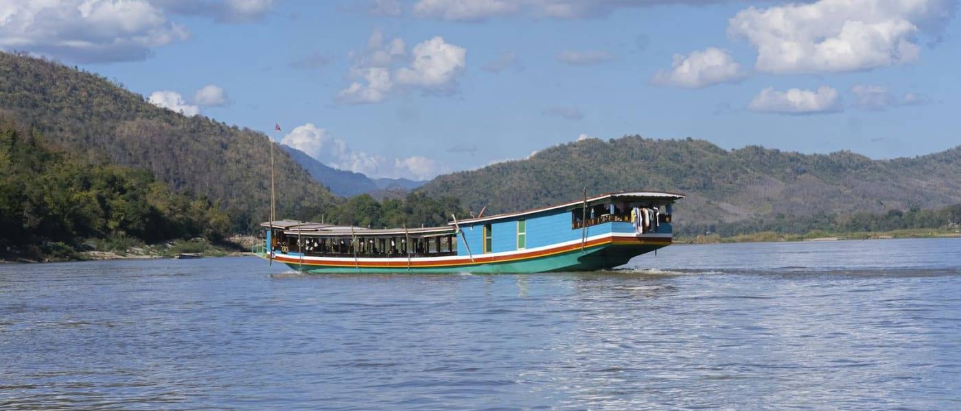 Slow boat on a wide river between green hills